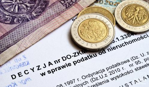 Na decyzji podatkowej leżą banknoty (20 złotych i 10 złotych) i monety (dwie monety po 5 złotych i 1 moneta 2 złotowa).