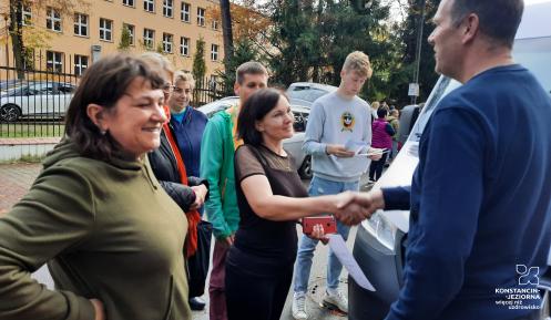 Kilka osób, jedna z nich, kobieta, podaje rękę mężczyźnie w geście podziękowania.