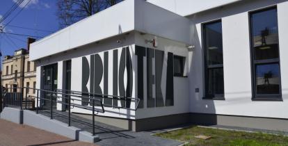 Przestrzeń miejska. Budynek biblioteki z białą elewacją i dużymi oknami.