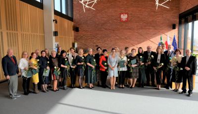 Sala konferencyjna. Dwadzieścia sześć osób stoi obok siebie w rzędzie – sześciu mężczyzn i dwadzieścia kobiet. Większość w rękach trzyma dyplom w zielonej teczce i białą różę.