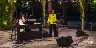 dwie osoby w altanie grają koncert, jedna siedzi za pianinem druga stoi i śpiewa