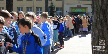 Dzieci i młodzież stoi przed budynkiem szkoły. 
