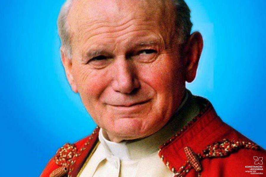 Starszy mężczyzna w stroju hierarchy katolickiego, okryty czerwonym płaszczem, na błękitnym tle